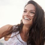 Brunette woman with permanent porcelain veneers smiles in Denver, CO
